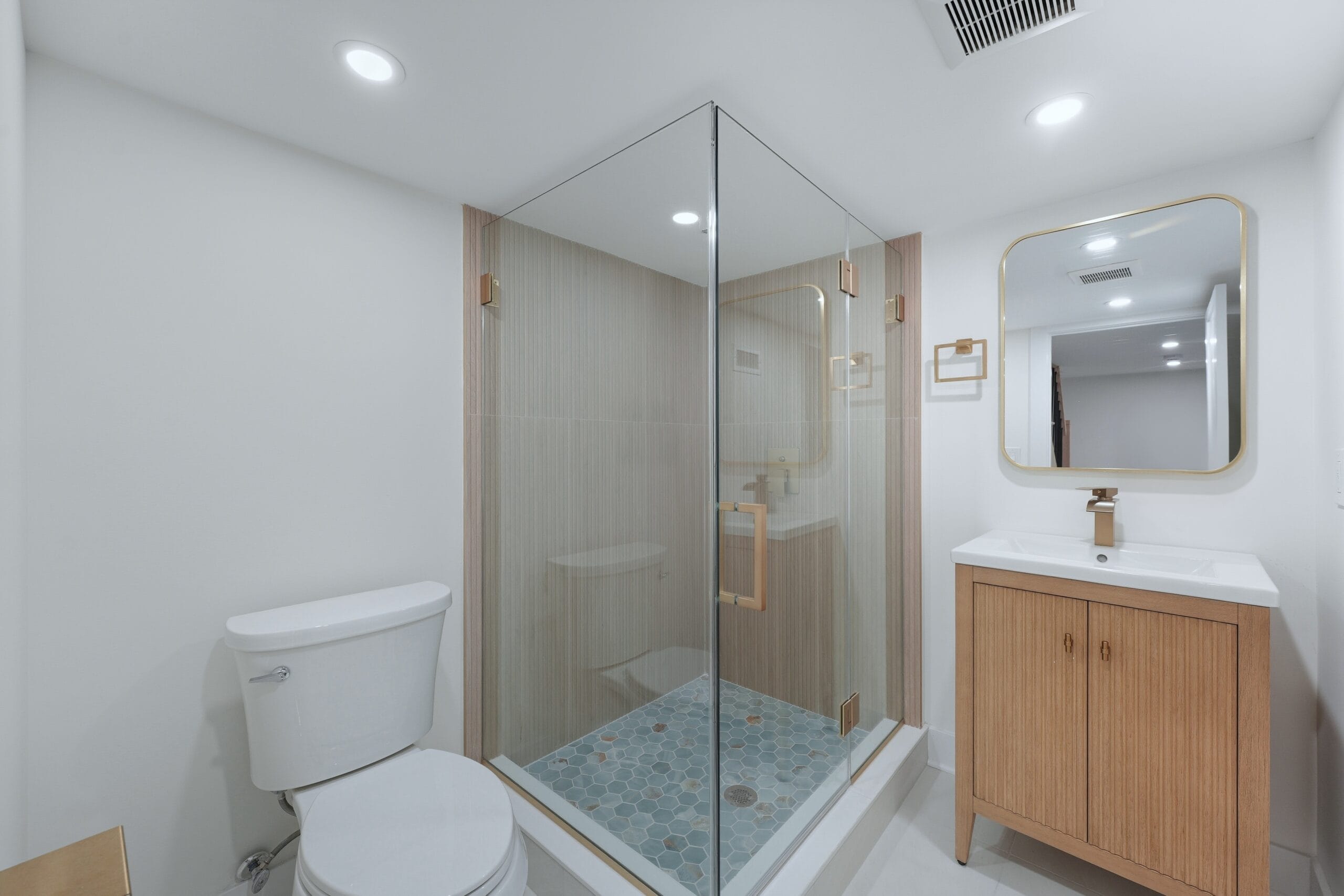 Guest bathroom with a frameless glass corner shower, blue penny-tile floor, and a fluted oak vanity