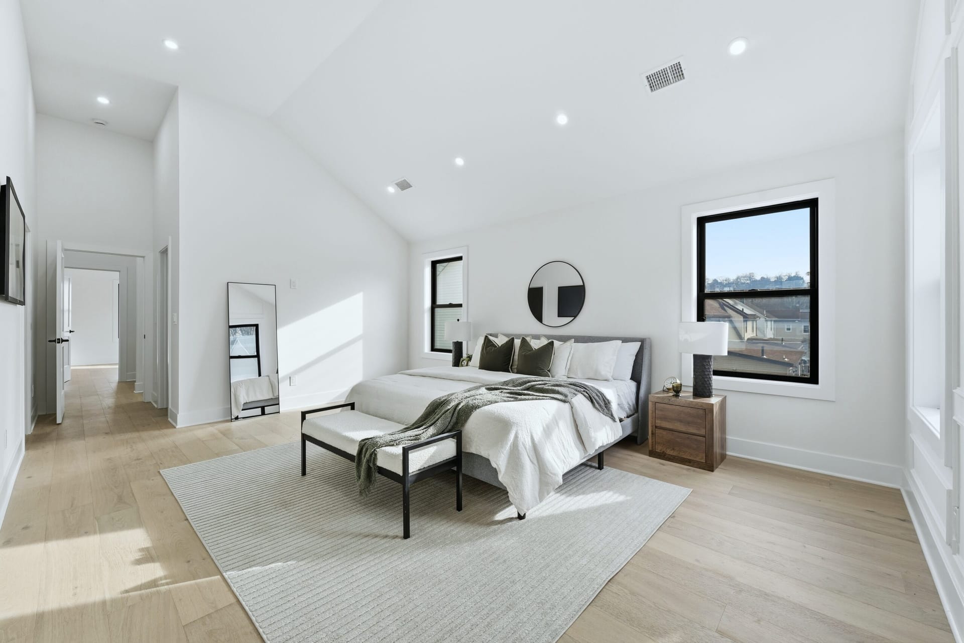 Primary bedroom with a vaulted ceiling, large black-framed windows, and warm staged furnishings