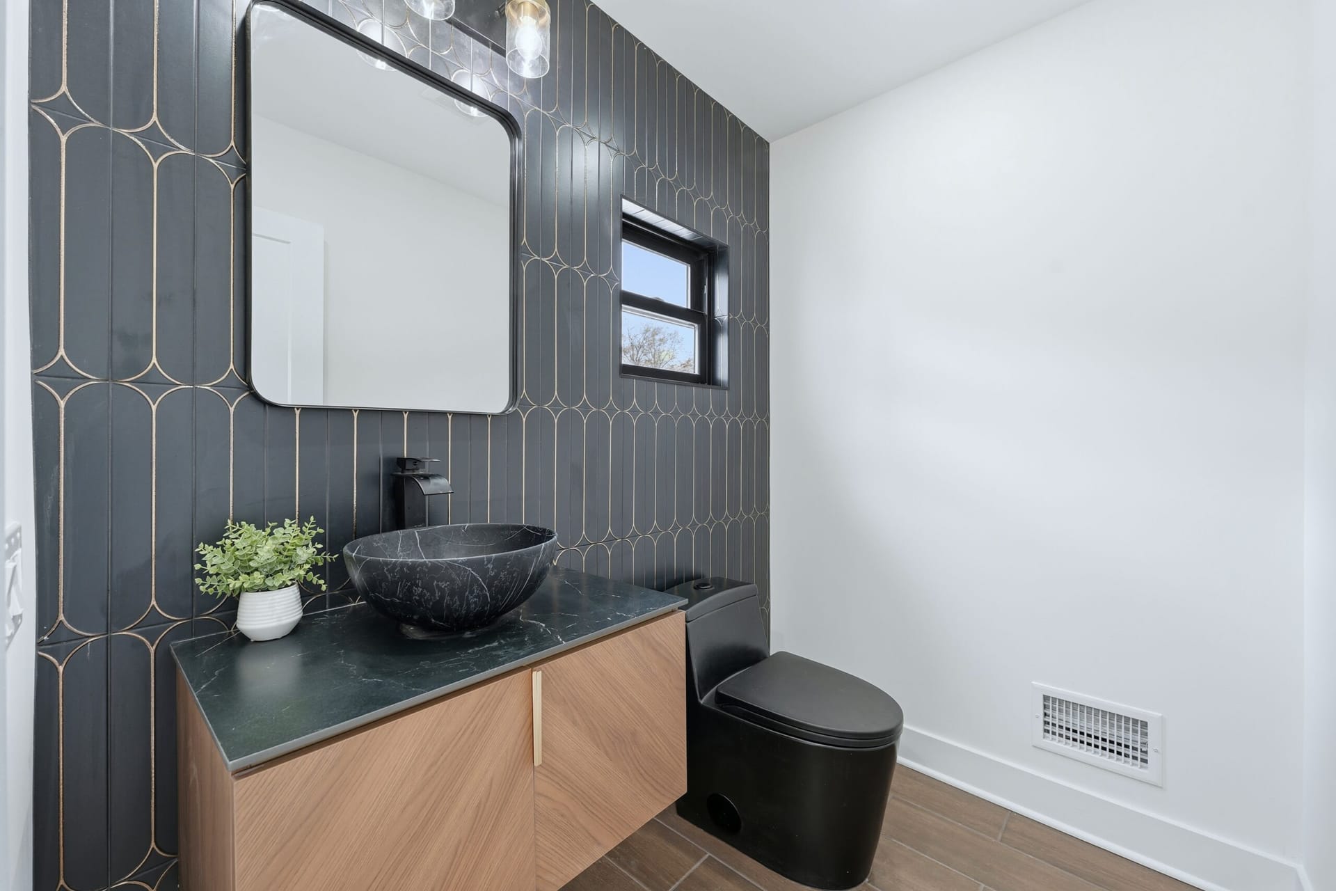 Powder room with deep green and gold art-deco wall tile, a black marble vessel sink, and a fluted oak vanity