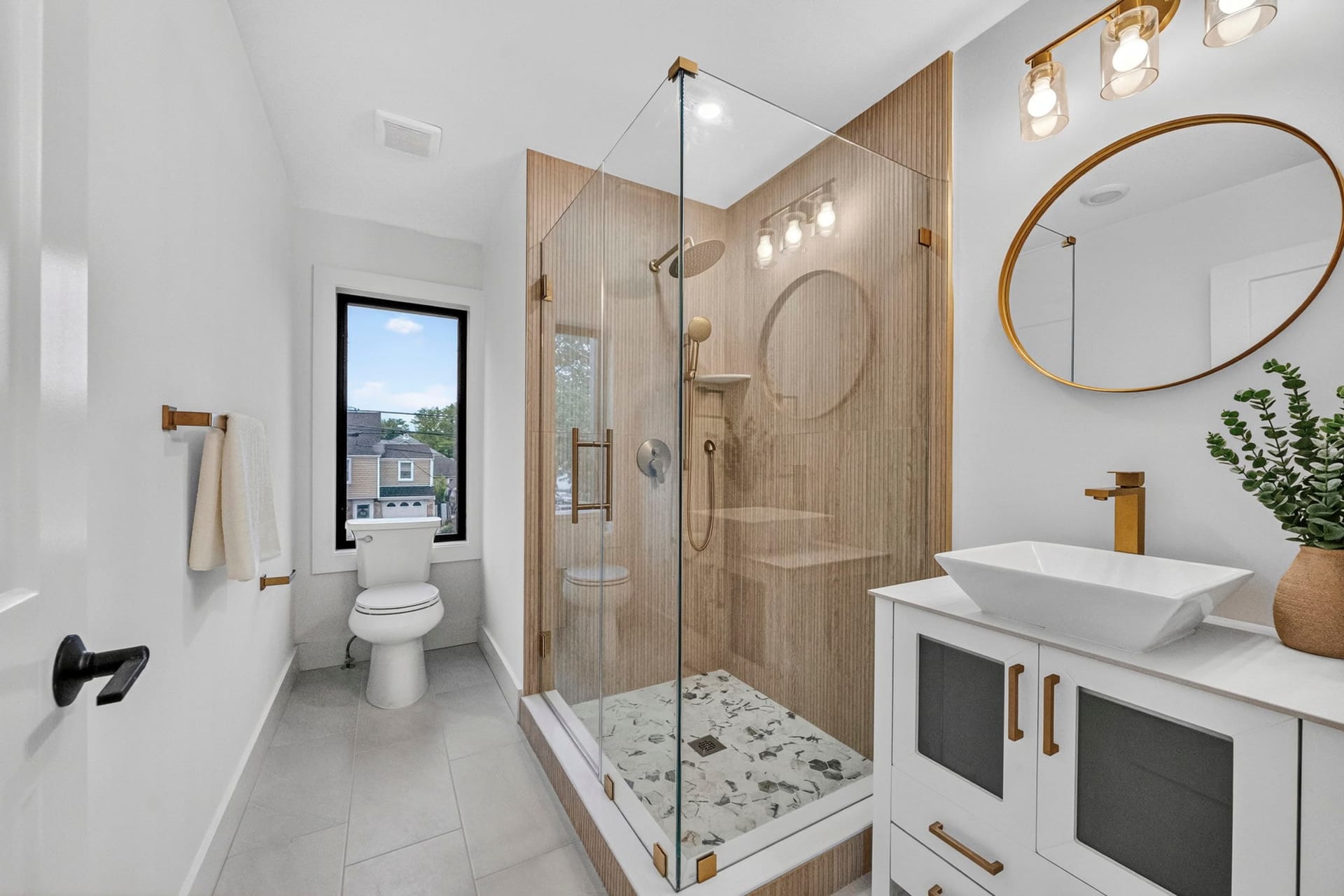 Bathroom with a glass shower, oval mirror, and a vessel sink with brass fixtures