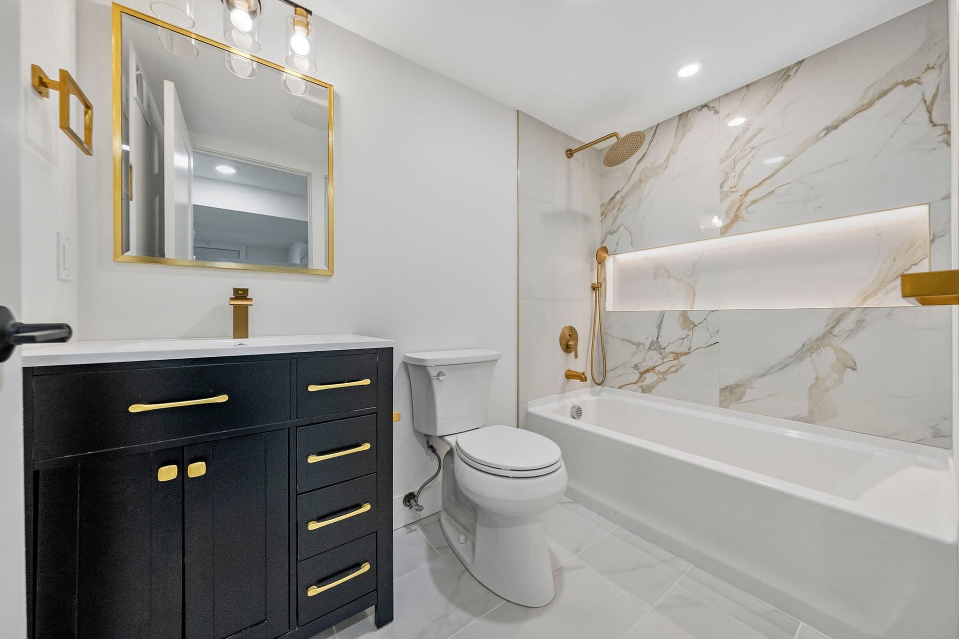Basement bathroom with a black vanity, brass fixtures, and a marble-look tub surround